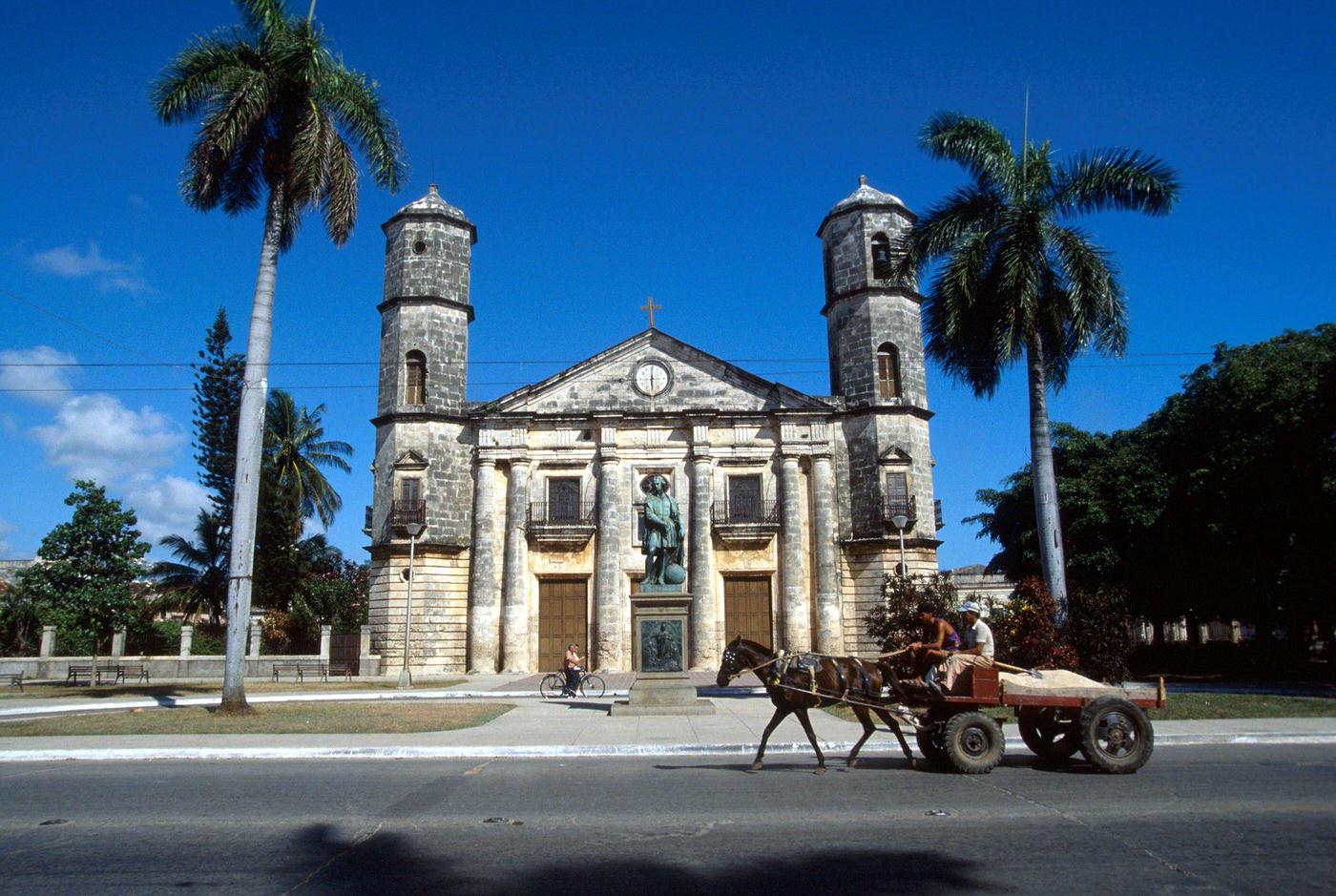 Two Cuban peasants driving a horse-drawn cart in front of the cathedral and monument in Cardenas, Cuba, 1990.