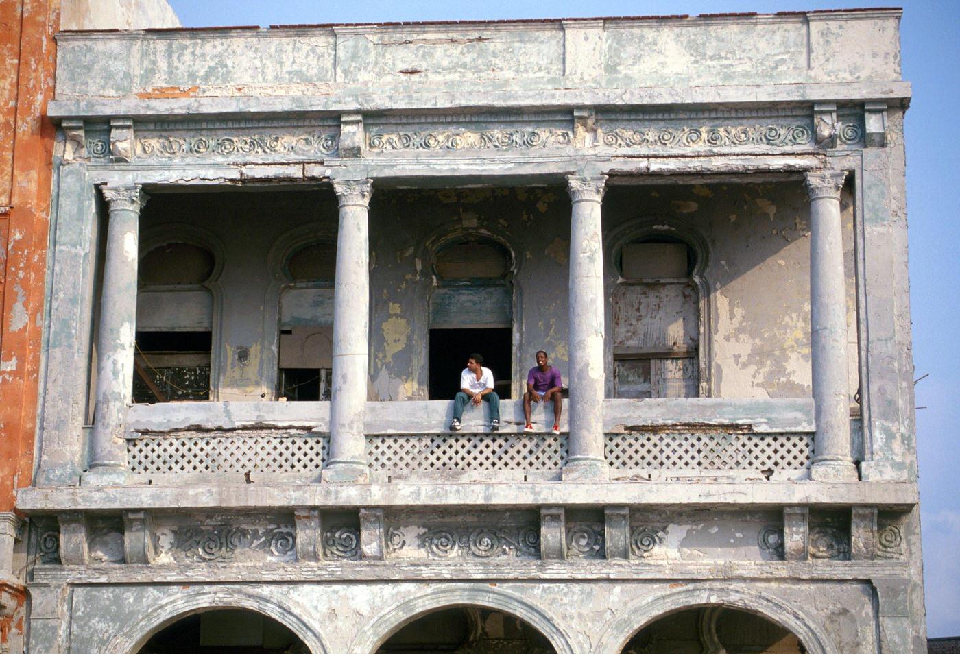 Two Cuban boys sitting on the balcony of a building along the Malecon promenade in Havana, Cuba, 1990.