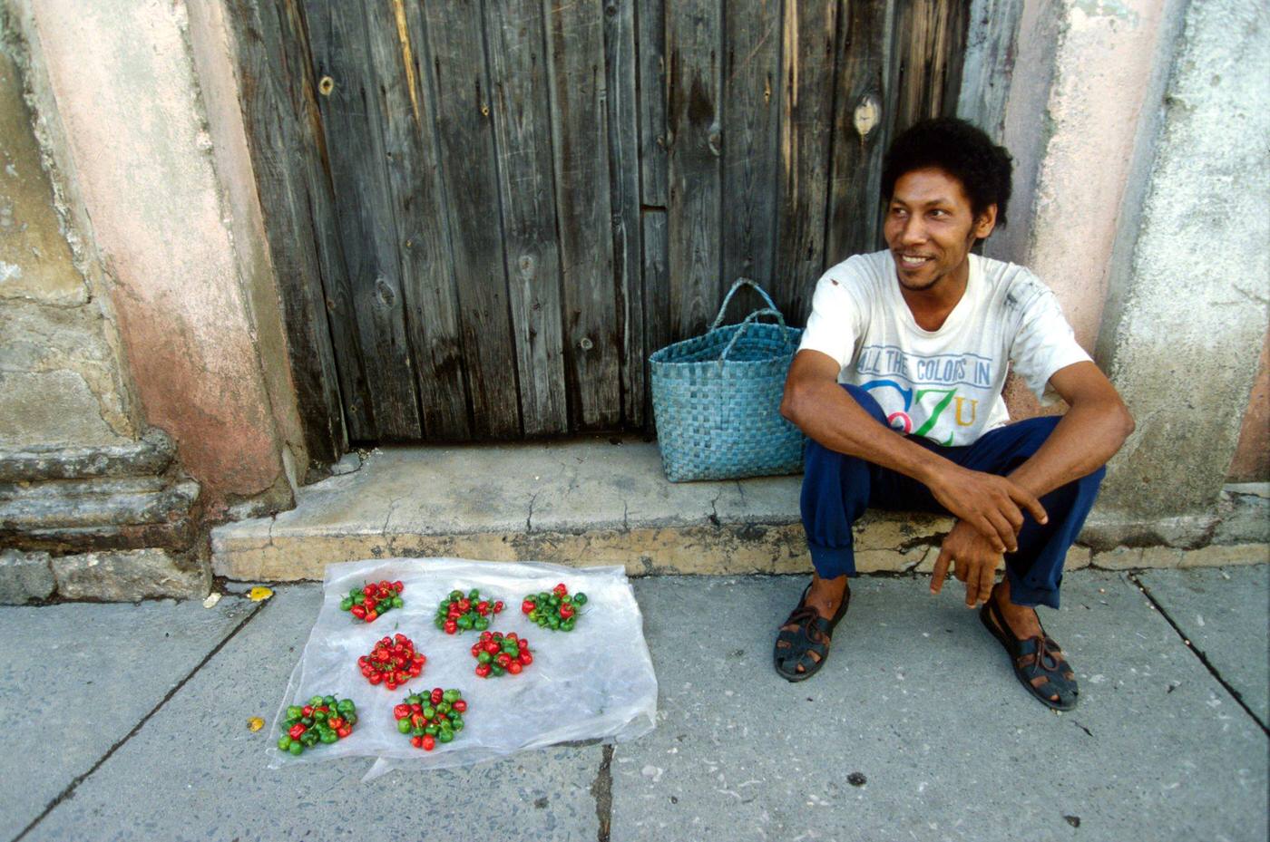 Cuban man selling chili peppers displayed on the pavement in the street, Cuba, 1990.