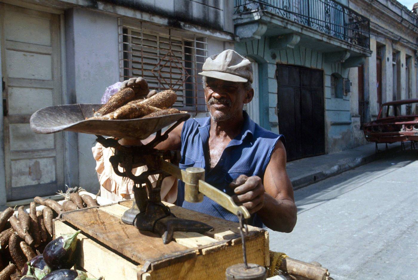 Cuban man weighing yucca to sell in the street on a scale, Cuba, 1990.