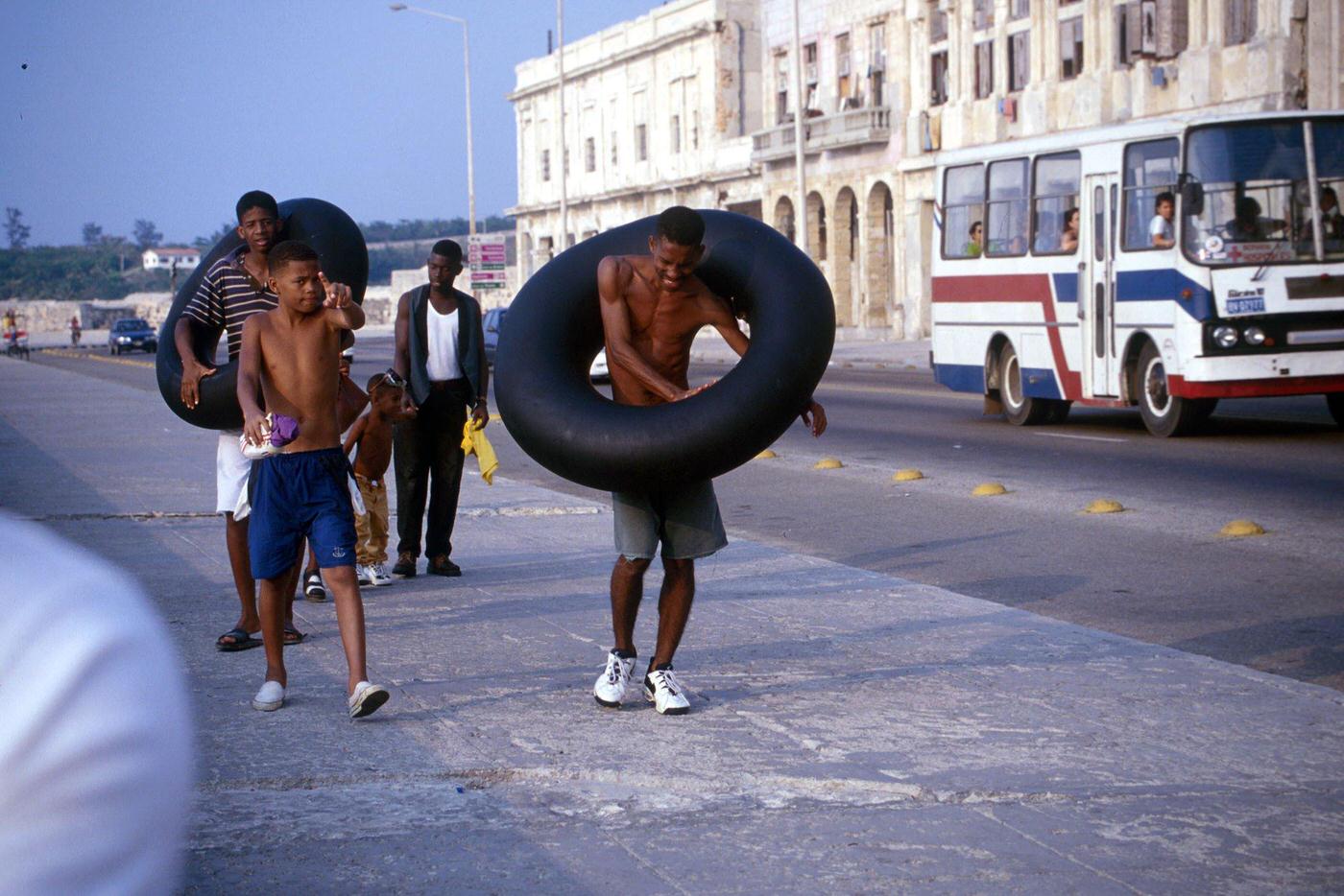 Cuban boys walking along Malecon promenade in Havana, carrying inner tire tubes, Cuba, 1990.