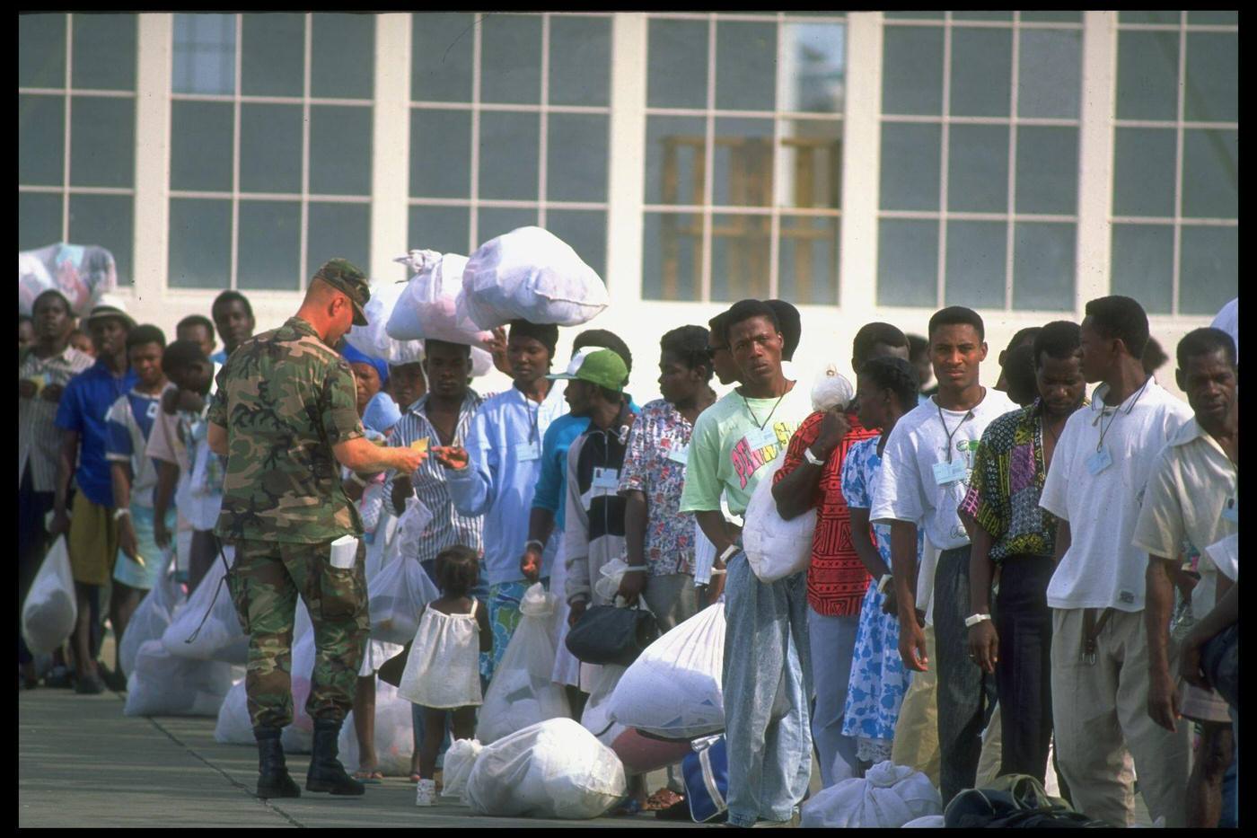 Haitian refugees picked up at sea by the Coast Guard lining up for processing at a US naval base camp, facing deportation/repatriation.