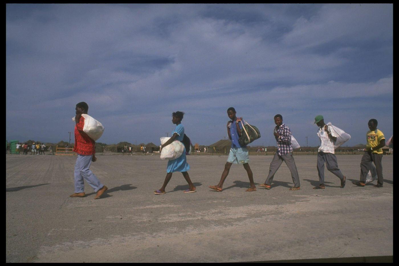 Haitian refugees picked up at sea by the Coast Guard arriving/leaving at a US naval base camp, facing deportation/repatriation.