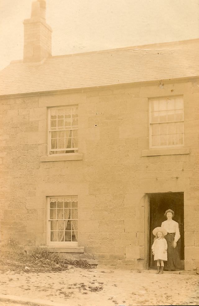 Mother and child stand in doorway of stone-built terrace house