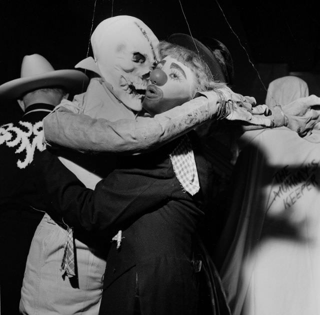 A ghoulish goblin and a painted clown embrace at a Halloween party in 1955.