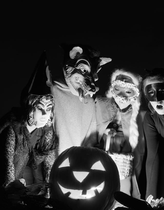 Four masked trick-or-treaters gather around a jack-'o-lantern in the 1960s.