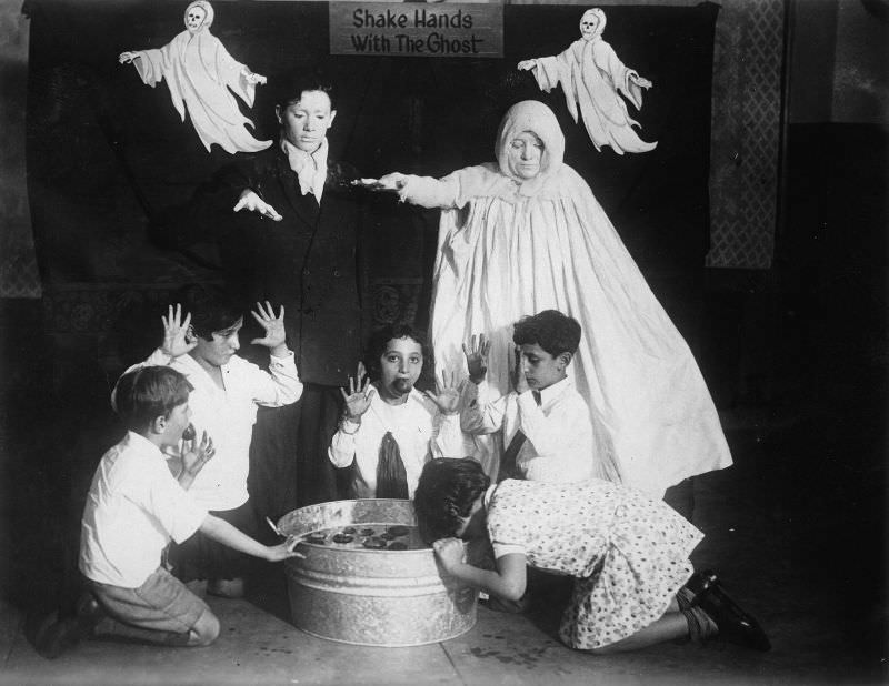 Children surrounded by ghosts go bobbing for apples at a Halloween party around 1935.