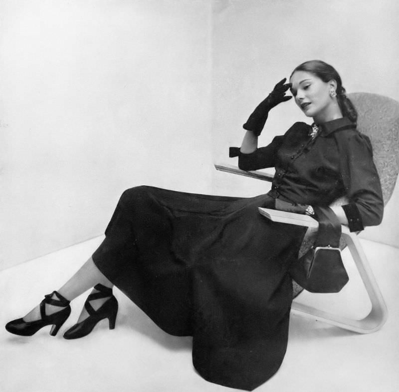 Marilyn Ambrose in tissue faille dress with velvet edges, velvet tie, belt and cuffs, fastened with tiny mock-jet buttons by L'Aiglon, shoes by I. Miller, chair by Saarinen, Vogue, 1947.