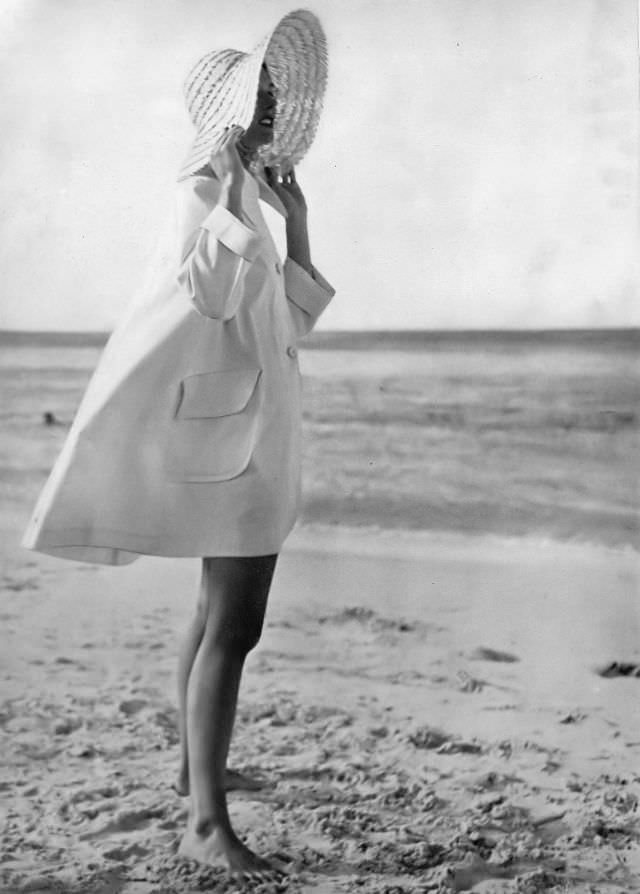 Model in sea-going topcoat of stiff white poplin with big collar and patch pockets by Sunclothes, at British Colonial Beach, Bahamas, Harper's Bazaar, 1948.