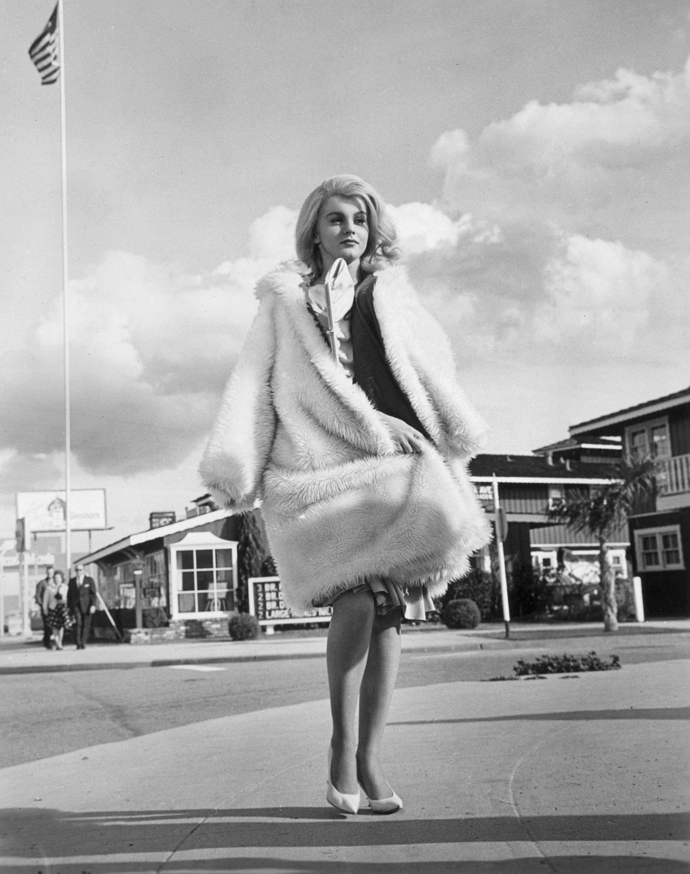 Ann-Margret wears a fake fur coat while walking on a sidewalk in a still from the film, 'Kitten With a Whip'.