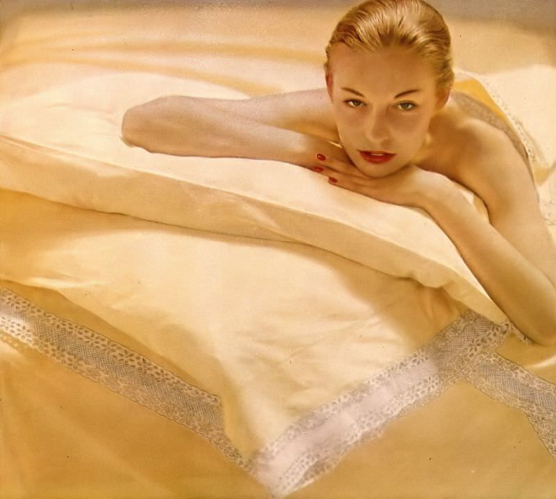 Liz Pringle lying on sheets the color of daffodils in Bates percale, pillowcases and blanket embroidered in white eyelet, by Carlin Comforts, Harper's Bazaar, October 1948