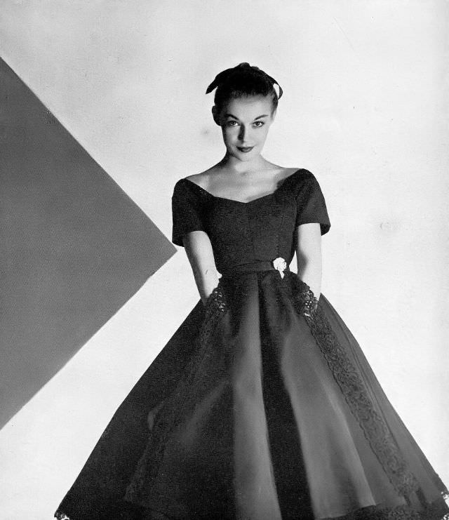 Liz Pringle in black silk bengaline dress scrolled with heavy black cotton lace at neck, hem and apron front, by Omar Kiam for Ben Reig, Harper's Bazaar, December 1951