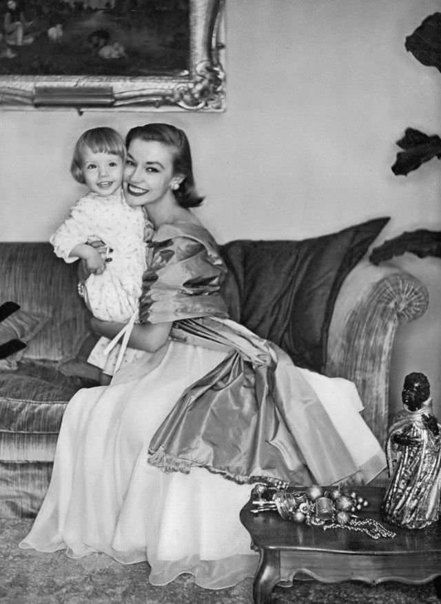 Liz Pringle in gown of white Italian silk chiffon over taffeta worn with grass-green taffeta stole by Eleanora Garnett, holding her two-year old daughter Shawn, February 15, 1953
