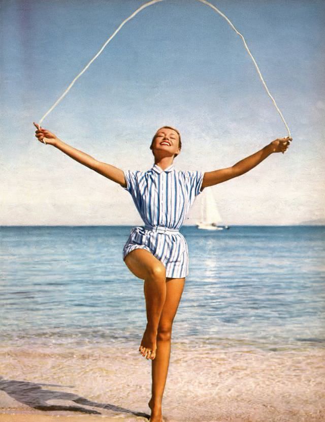 Liz Pringle in striped cotton jersey beach shirt belted and hip-pocketed over a suit of the same cotton by Brigance of Sportmaker, May 1956
