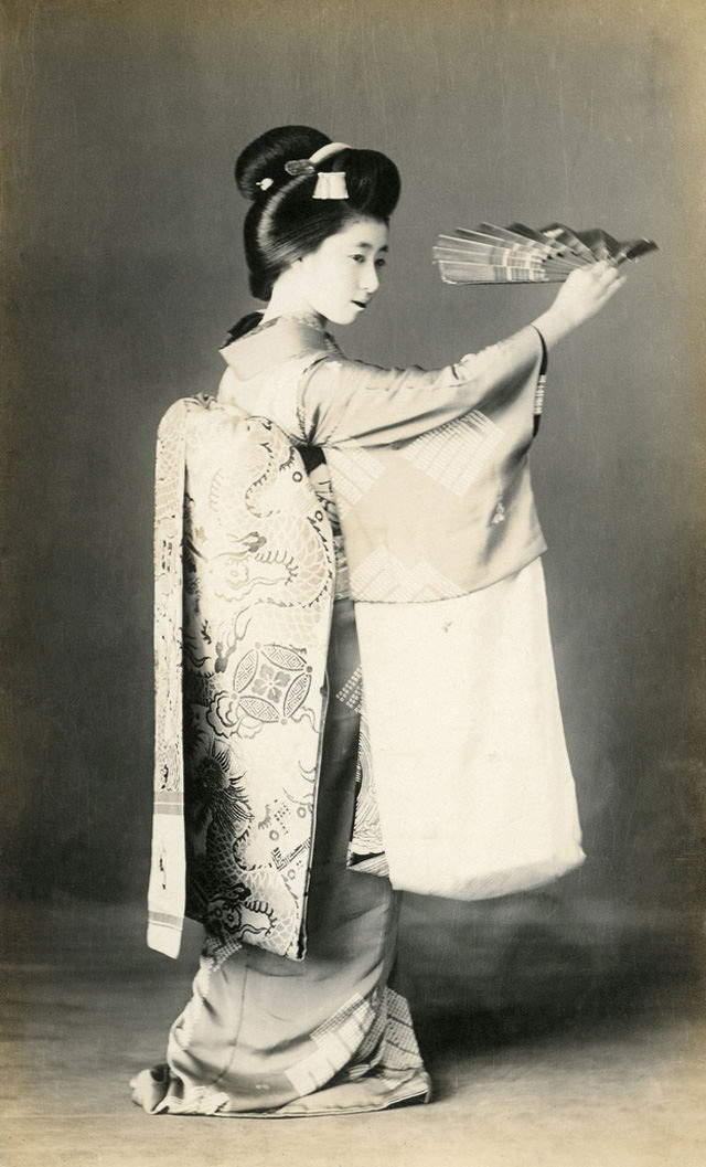 Maiko dancing with a mai-ogi (dancing fan), her obi (sash) decorated with dragons and pearls, 1910s