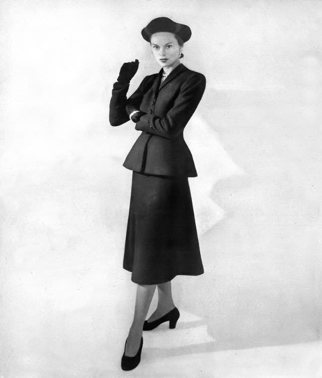 Meg Mundy in black wool suit with a curved jacket that bells out above a rippling skirt by Hattie Carnegie at the Lindner Coy, Harper's Bazaar, September 1947