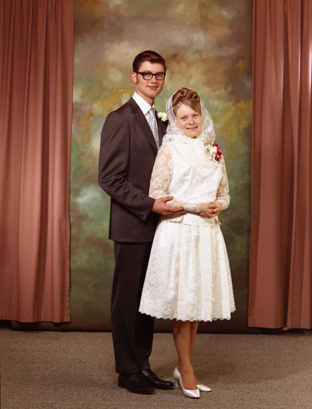 Wedding portrait of a Doukhobor couple. The groom is wearing a brown suit, with a white shirt and silver tie. The bride is wearing a knee-length white dress, a corsage, and a traditional white headscarf, May 8, 1971