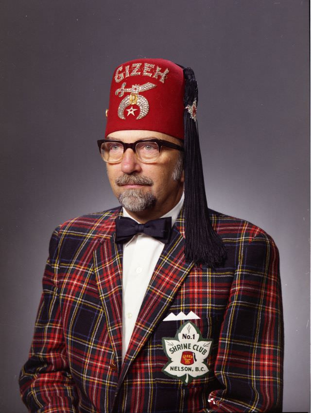 George Roland Zubick in Shriner dress. He is wearing a red, tasseled hat with with the word "GIZEH", a plaid suit jacket that has a patch attached to it which reads "No. 1 Shrine Club Nelson, B.C.", September 23, 1972