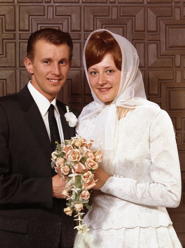 Doukhobor wedding portrait of John Kooznetsoff and Christine Posnikoff. The couple are both holding a bouquet of pink-and-cream flowers, April 25, 1970