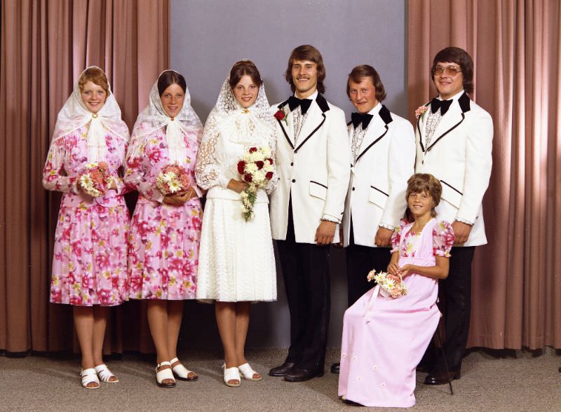 A group wedding portrait of a Doukhobor couple. The image contains four female figures and three male figures. The bride is wearing a white dress with a white headscarf, July 26, 1975