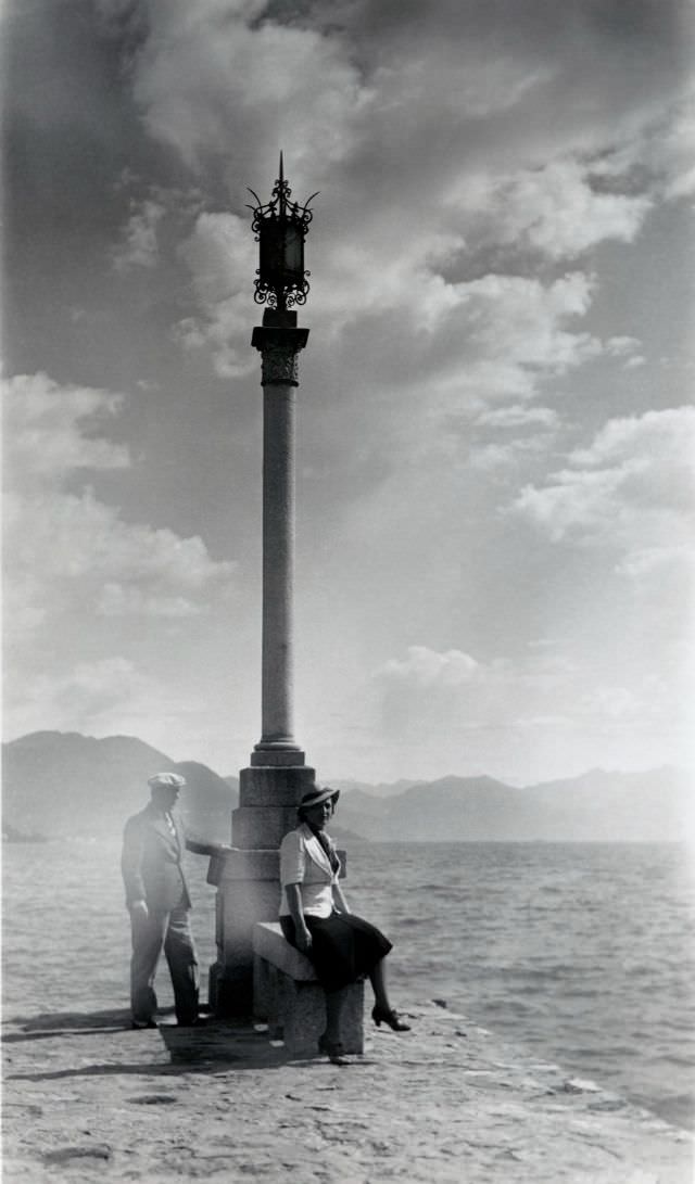 A stylish couple posing next to an elaborate lamp post at the waterfront, 1935
