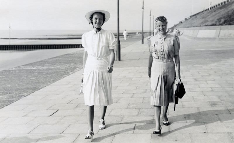 Two fashionable ladies strolling along a seafront promenade on a sunny summer's day.