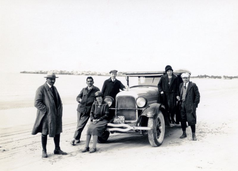A company of six posing with a 1926 Studebaker Phaeton on a beach in wintertime, December 9, 1927