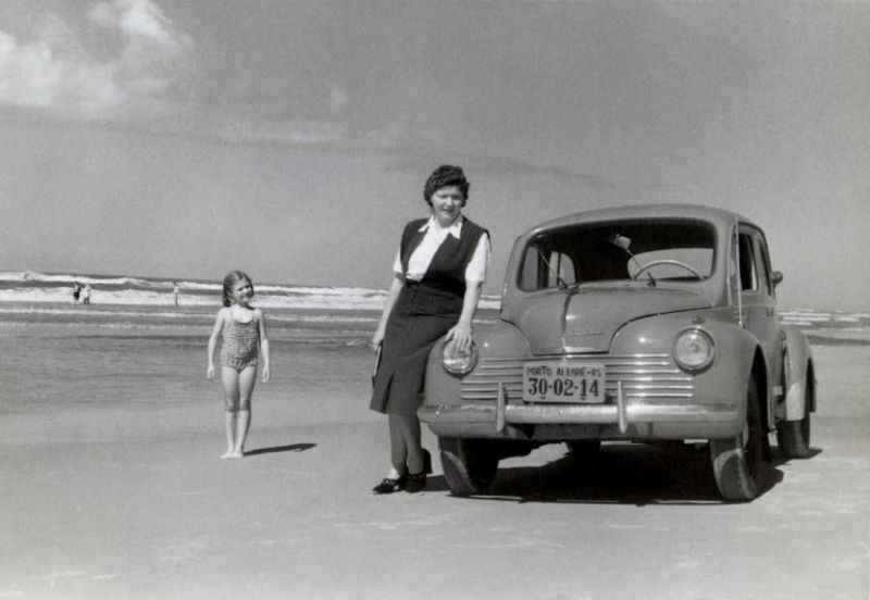 A mother and her daughter posing with a Renault 4 CV on a beach in bright midday sunshine, April 1952