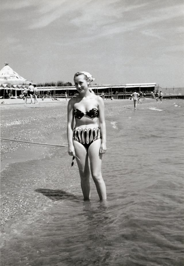 A blonde lady in a two-piece swimsuit posing on a sunny beach, 1950s