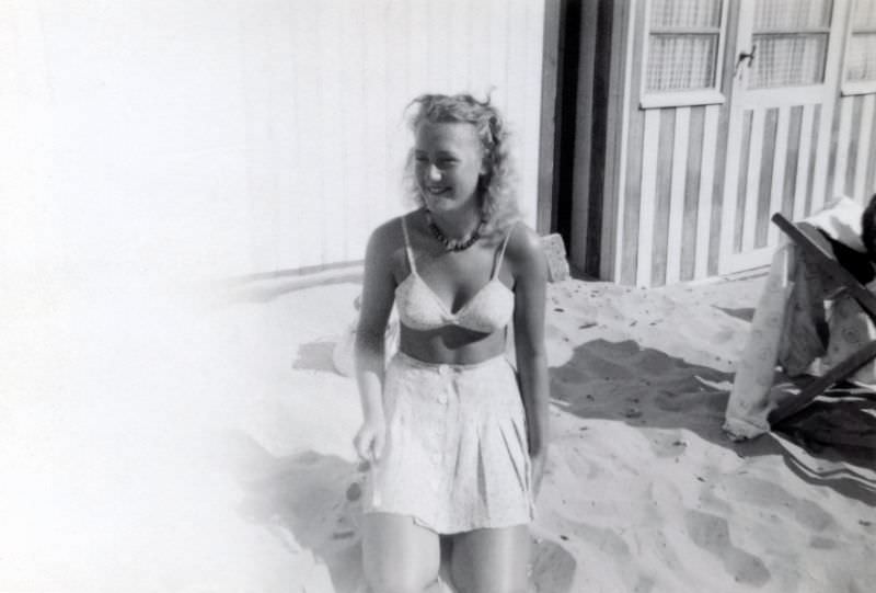 A cheerful blonde lady in a two-piece swimsuit posing on a beach in summertime, 1950s
