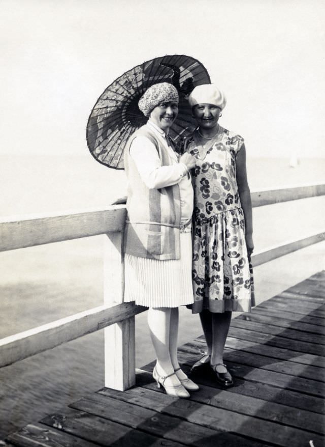 Two cheerful ladies posing with a parasol on a wooden pier overlooking the Baltic Sea, 1928