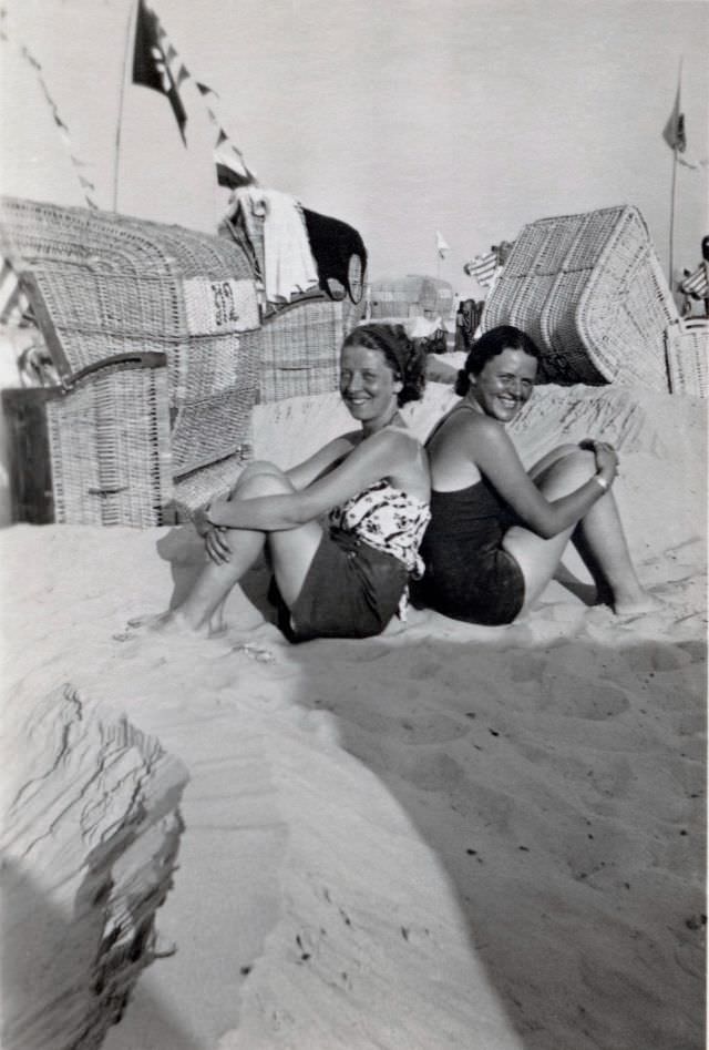 Two cheerful young ladies posing on a sandy beach, suntan in progress.