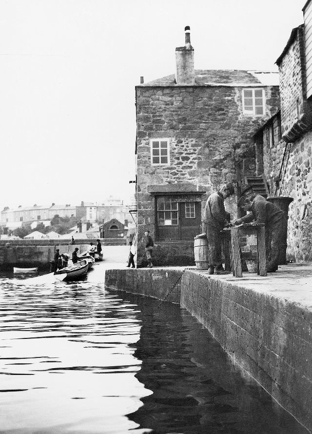 A view of the wharf with some fisherman occupied with a task at a crude bench/table, St. Ives, Cornwall