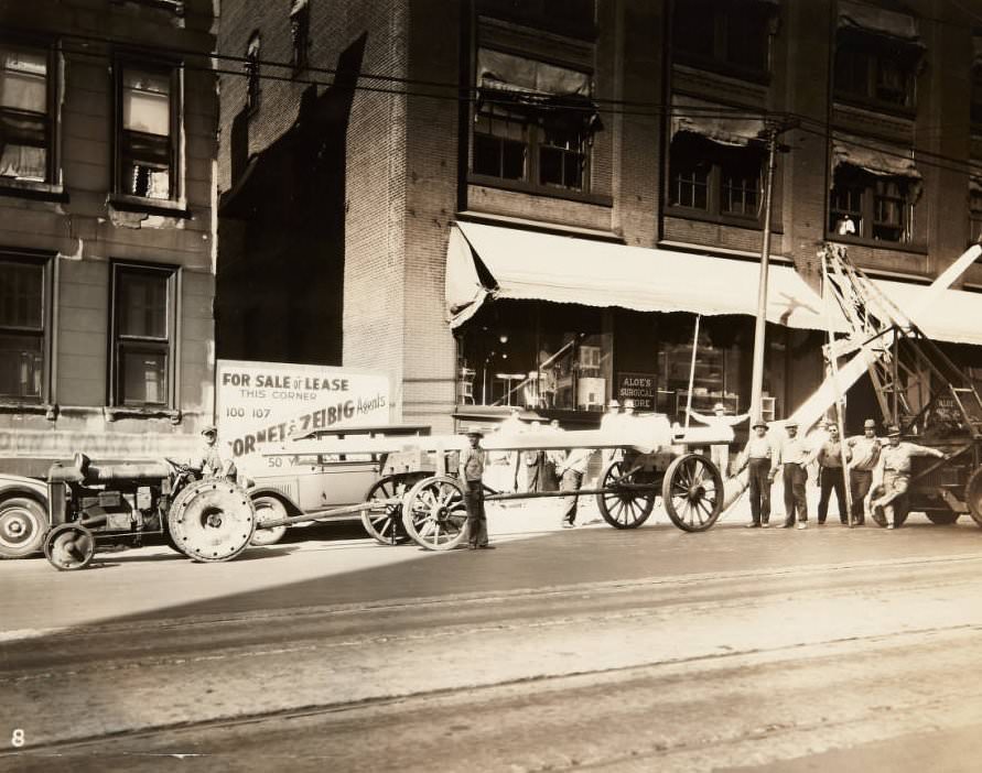 Workmen posing next to the posts they are installing for street lights on the 1800 block of Olive Street in 1920. The storefront for Aloe's Surgical Store can be seen behind them.