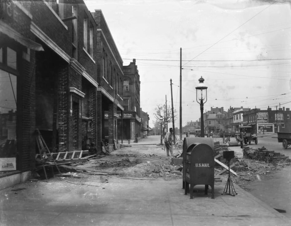 North view on North Grand Blvd. near Palm Street, with street laborer near piles of bricks and businesses such as E. F. Schulte Hardware Co., B. Kolbenschlag, and Hohengarten bakery visible, 1925