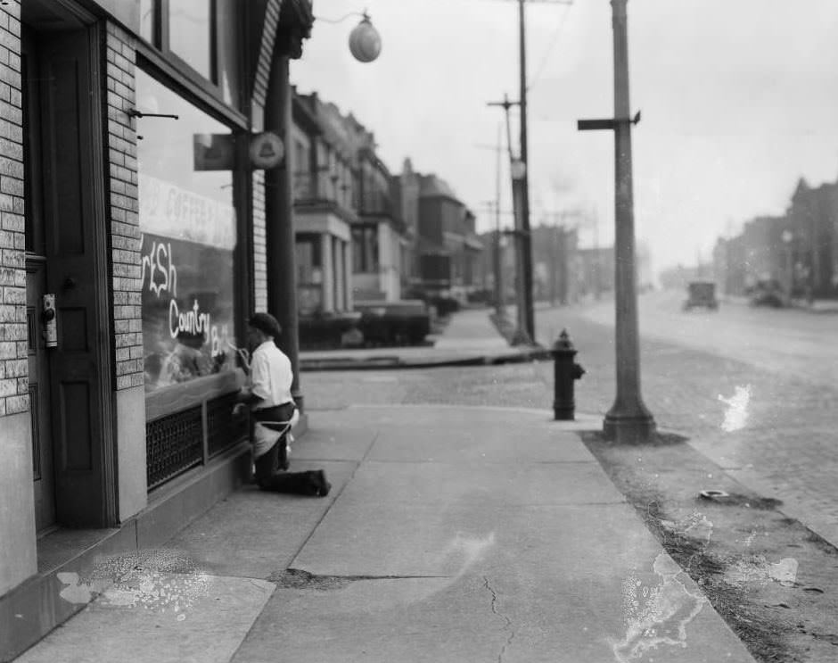 East view down Arsenal Street at the intersection with South Compton Ave., with building 3201 Arsenal Street on the left and a man painting "Fresh Country Butter" on his business window, 1925