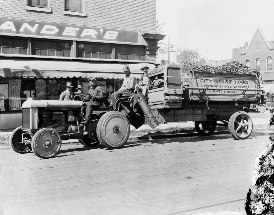 View of a City of St. Louis, Department of Streets and Sewers, Sewer Division tractor and refuse truck and crew on South 39th Street, in front of Rheinlander’s Dry Goods store, 1925