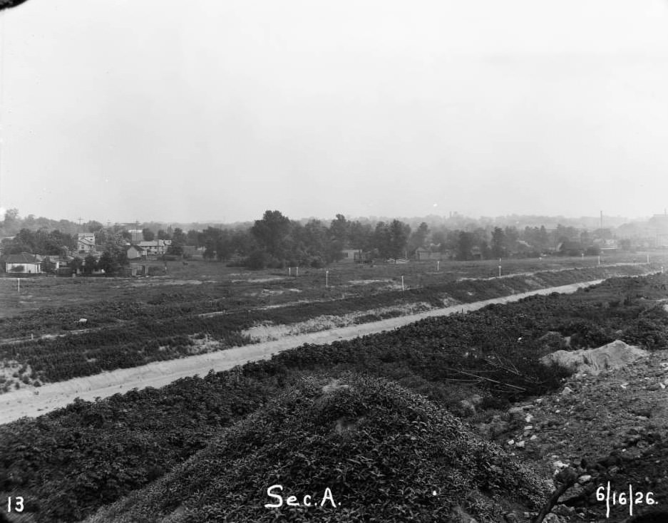 River Des Peres canal basin in what is now Ellendale, St. Louis, Missouri. Several homes and fields are visible beyond the canal, and Scullin Steel Co. factory building is in the background, 1926