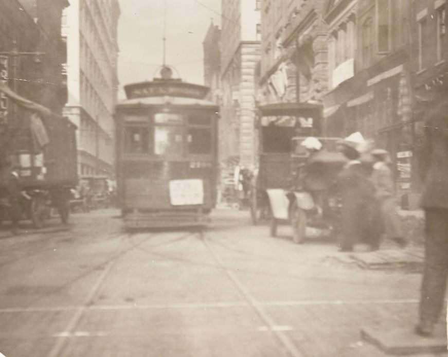 Daily streetscene of downtown St. Louis, likely on Pine Street, with a street trolley and automobiles visible, 1920