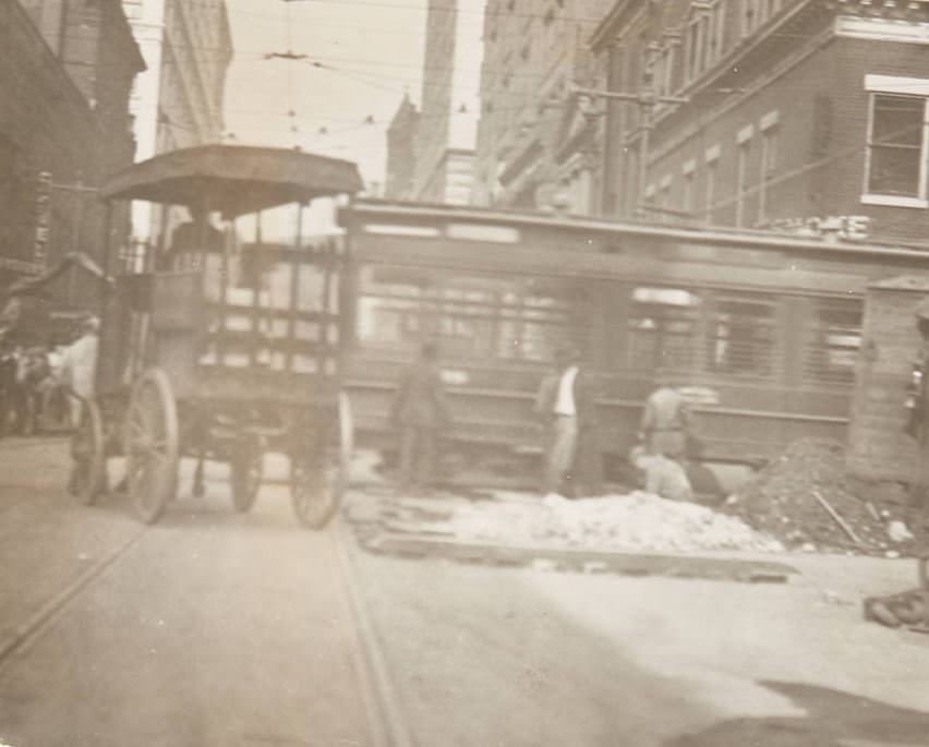 Street repairmen at work, likely near Pine Street downtown with a street trolley in the background and a work cart laden with bricks parked next to the repair site, 1920