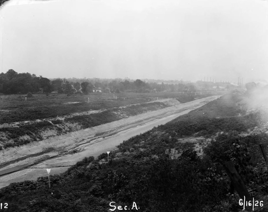 View of River Des Peres canal basin in Ellendale, St. Louis, Missouri, with fields flanking the canal in the foreground and factory stacks visible in the background.