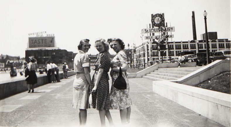 Women posing for a picture near Aloe Plaza. The St. Louis Dairy building can be seen in the background, 1940