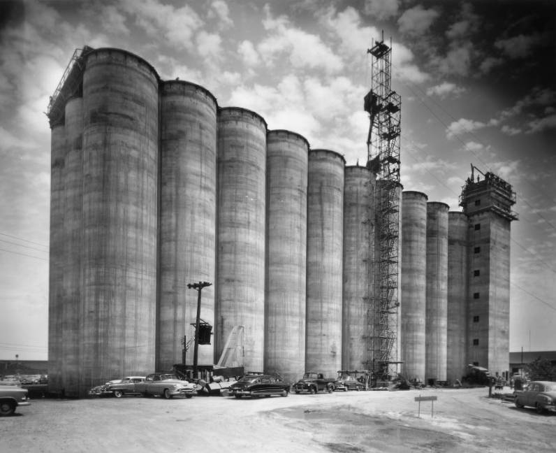 Exterior outdoor view of the Grain Silo with parked cars, 1954