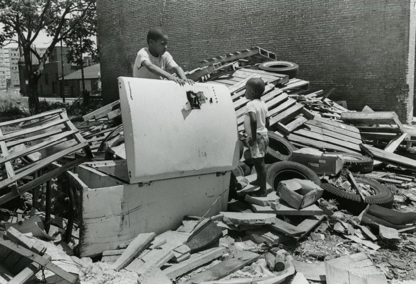 Two children search through debris left by a building after it was destroyed, 1970