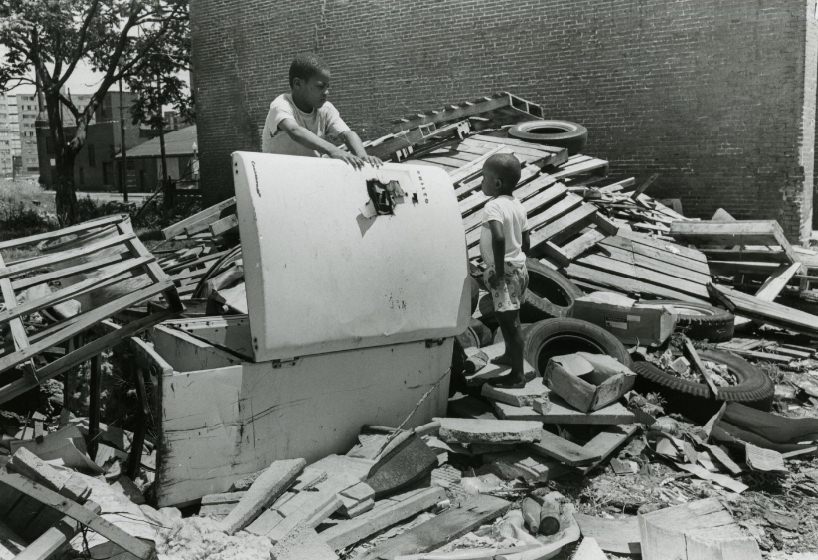 Two children search through debris left by a building after it was destroyed, 1970