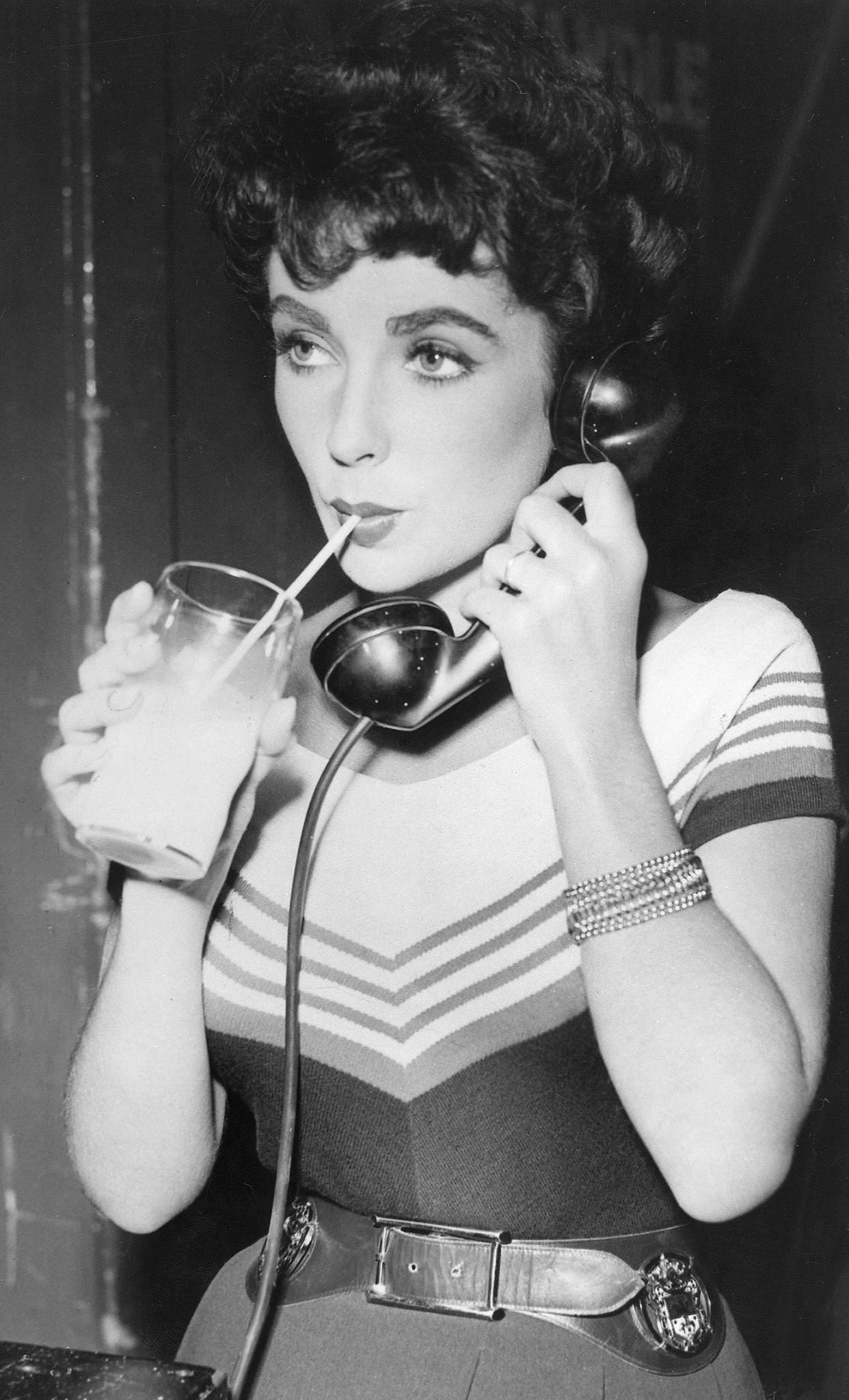 Elizabeth Taylor with a phone and milk glass during the filming of 'Girl Who Had Everything' (1953), USA.