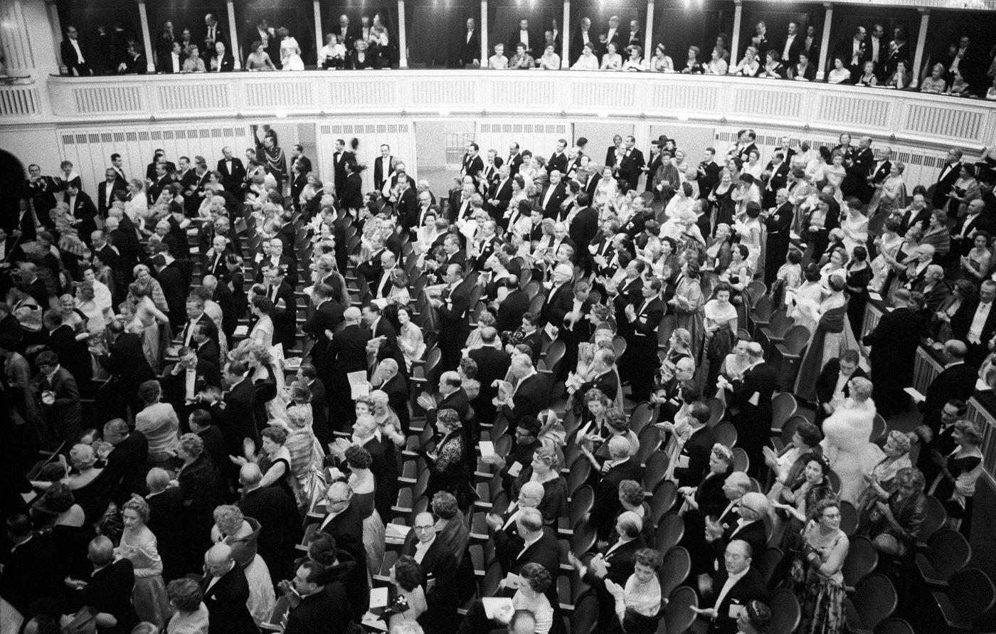 A crowd of people wearing gala clothes attending the reopening of the Vienna State Opera from the stalls in November 1955.