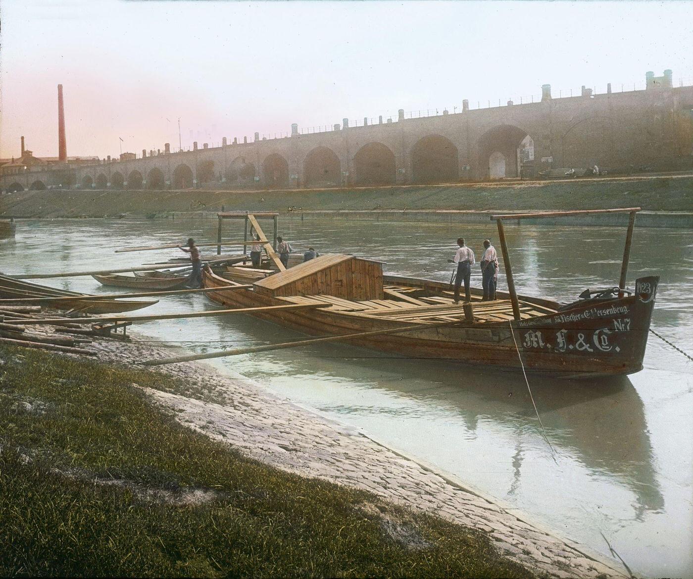 Unloading lumber from a barge at the Brigittenauer Laende, with a view of the Viennese Stadtbahn on the opposite bank, 1905.