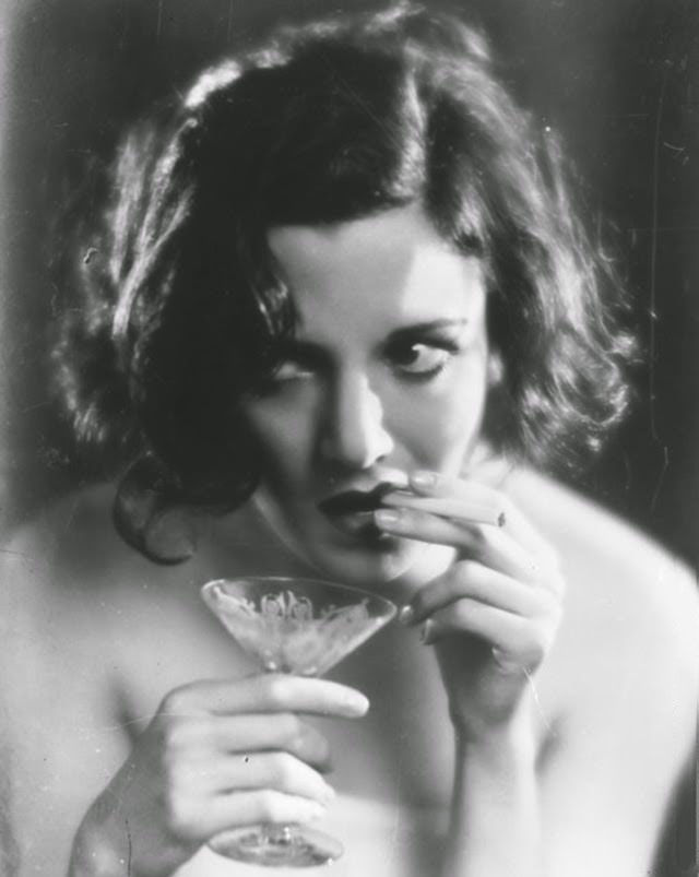 A woman smokes a cigarette while holding a cocktail glass in the other hand, 1929