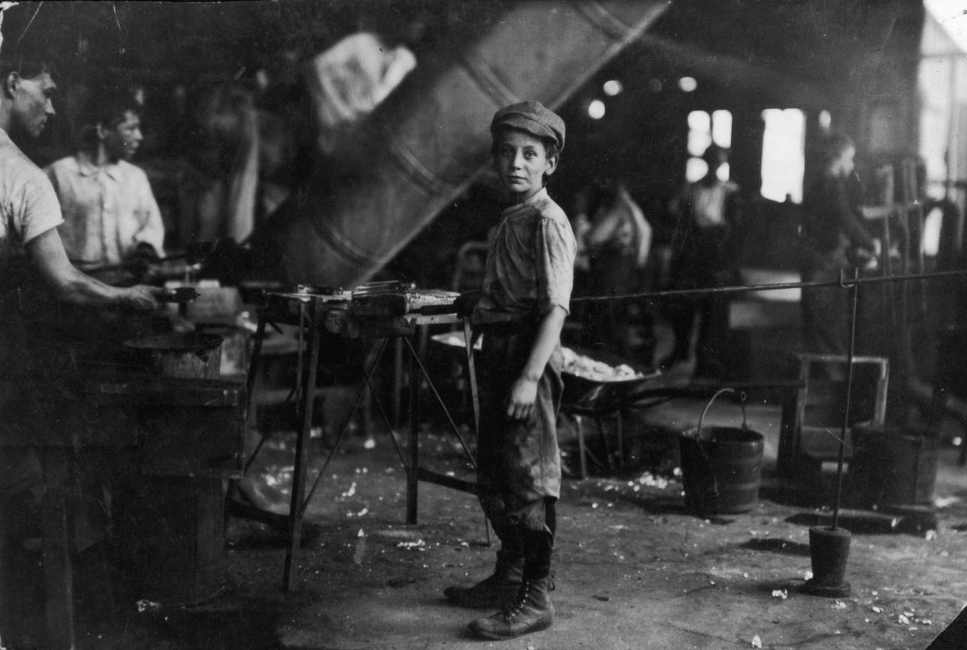 Aboy standing near men on the floor of a glass factory, Alexandria, Virginia, 1911